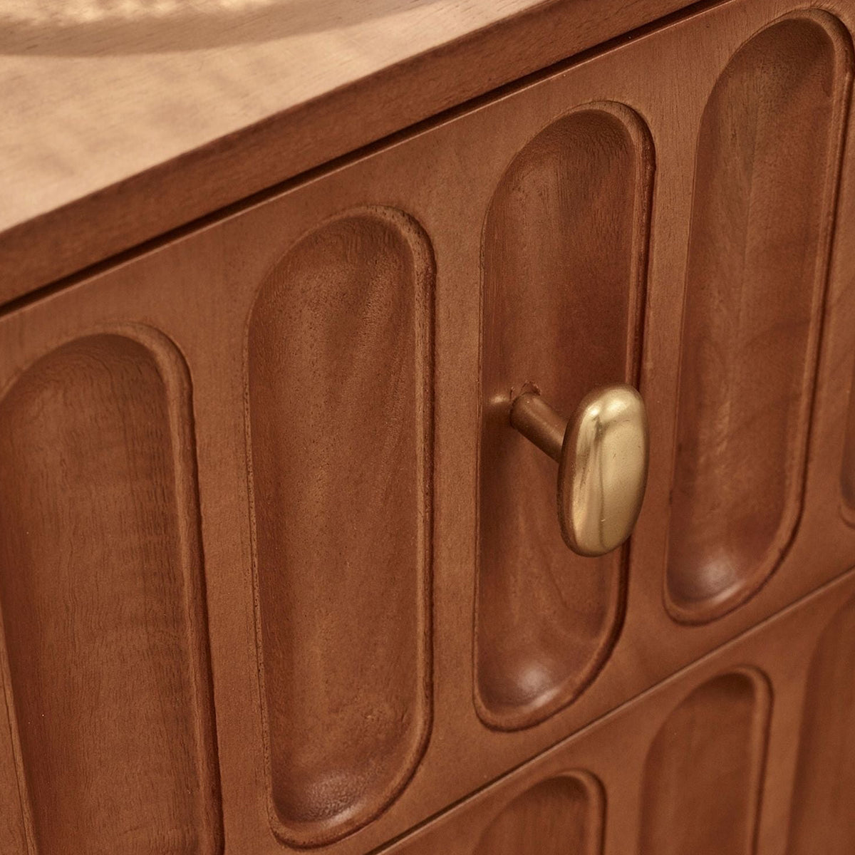 Close-up of a warm medium-brown wooden dresser or cabinet with vertically oriented oval recessed panels and round brass drawer pulls.